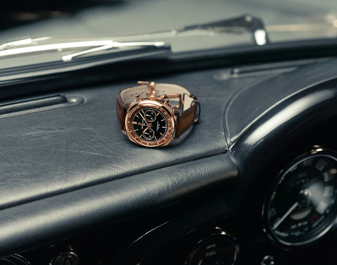 자동차 대시보드 위에 놓인 레드 골드 Breitling Top Time Aston Martin DB5